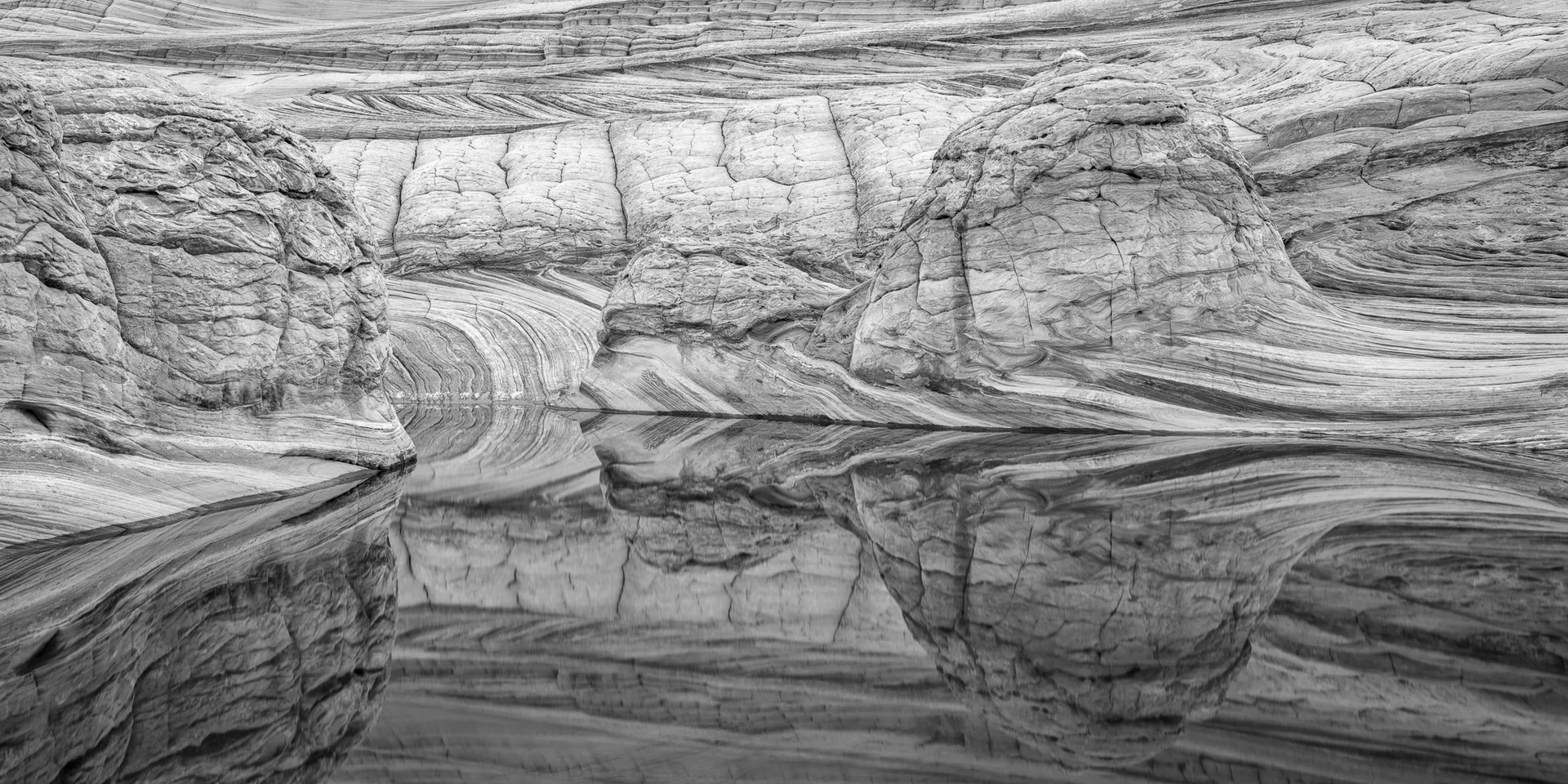Swirling cross-bedded sandstone and its mirror image in a still desert pool — geology and reflection become nearly indistinguishable, Arizona. Photograph by Marty Quinn